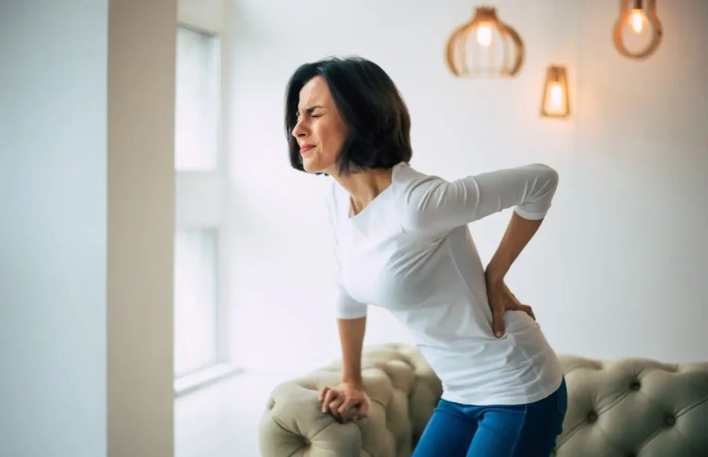 Mulher branca com a mão nas costas sofrendo com dores precisando de tratamentos para fibromialgia