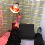Aplicação de luz infravermelha na fisioterapia na perna de um paciente, com lâmpada e eletrodos visíveis.